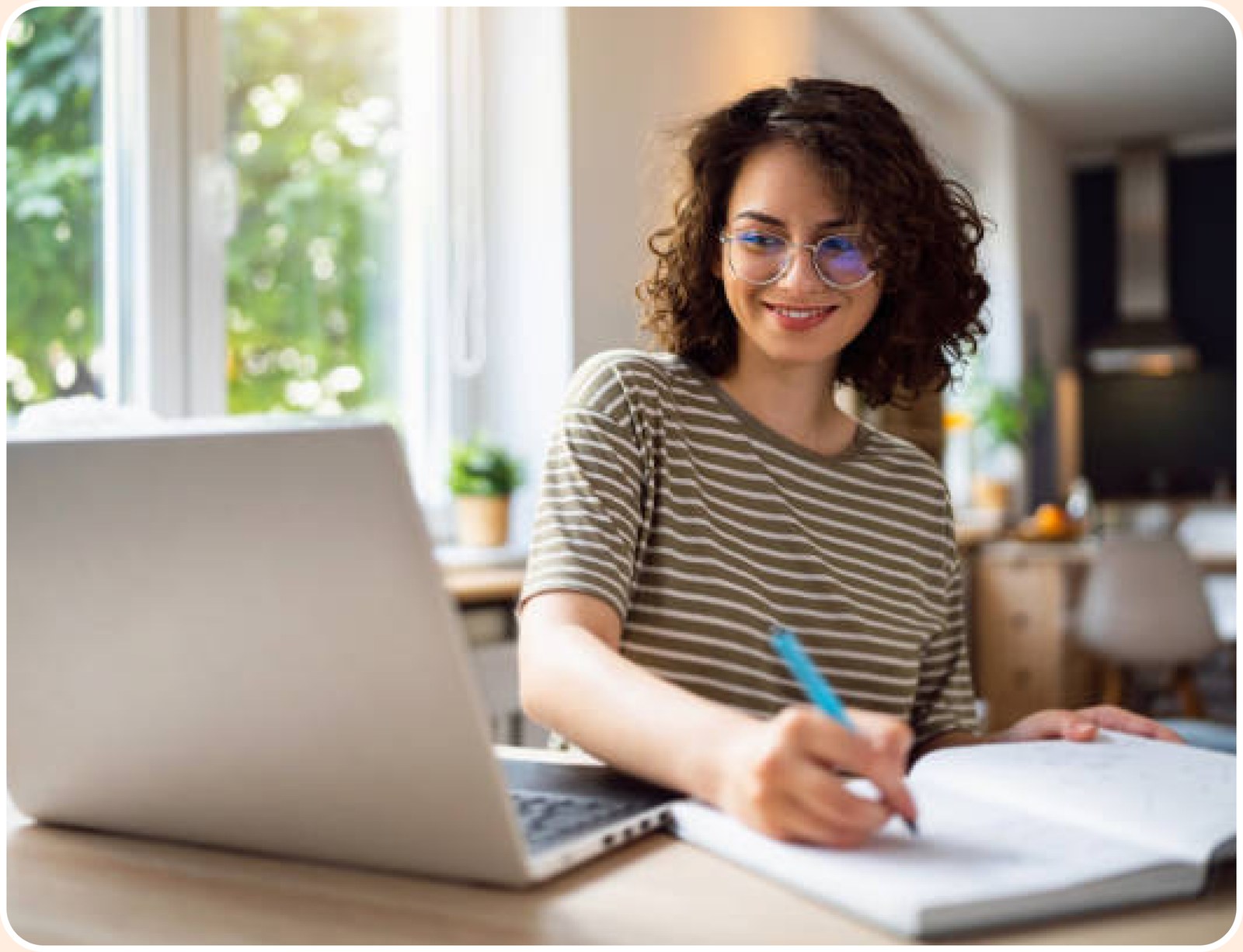 Student writing notes beside a laptop